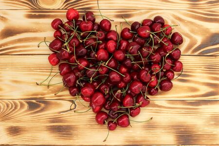juicy, sweet, ripe, fragrant cherry berries are piled on a textured wooden surface in the shape of a heart, a symbol of love. Gift beloved on Valentine's Day. Organic ecological natural dessert. Ingredient for baking and pie, original decorationの写真素材