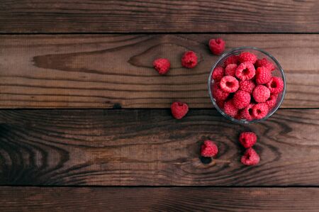 Red fresh raspberries on brown rustic wood background flatlay style. Bowl with natural ripe organic berries on planks, top view, with copy space. Fresh garden or forest harvest ready to eatの写真素材