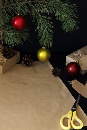 Christmas gift wrapping process. An empty sheet of craft paper lies on a table for packing a gift. Fir branch decorated with shiny colorful balls and cones on the background. copy space Happy new year themeの写真素材