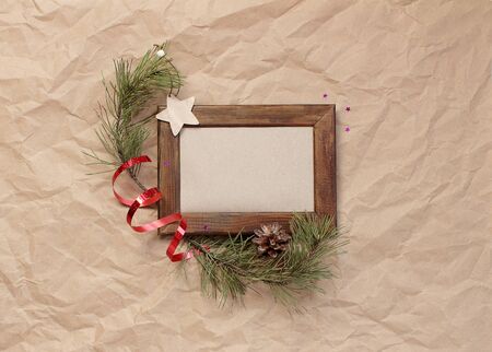minimalistic christmas composition. Wooden photo frame on craft paper background with Christmas tree branches, decorations, pine cones, sparkles stars. top view, copy space, happy new year conceptの写真素材