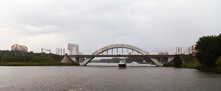 Cruise ship sets sail on the river under the arc-shaped bridgeの写真素材