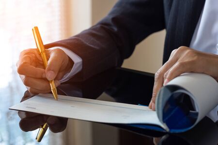 Business woman hand writing and signing blank checkbook on the table at modern office.の写真素材