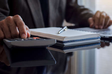 Closeup businessman hand using calculator and work on laptop computer with paperwork on the desk....