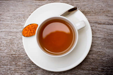 Closeup white ceramic cup of hot Turmeric tea with tumeric powder in metal spoon isolated on wood table background . Healthy drinks and health food boost immune system concept. Top view. Flat lay.の写真素材