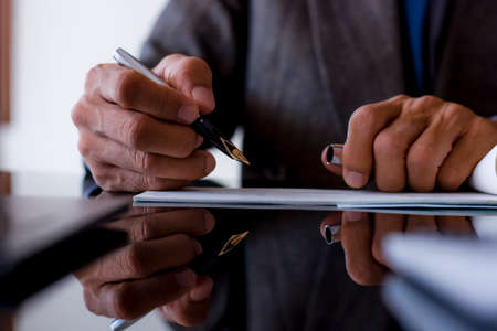 Business man in suit, hand writing and signing checkbook on the dark mirror table at modern office. Paycheck concept. Payment by cheque. Copy space with reflection.の写真素材