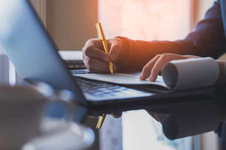 Business woman hand write and sign cheque book with laptop computer on the desk at office. Check payment, paycheck and payroll conceptual. Dark tone.の写真素材