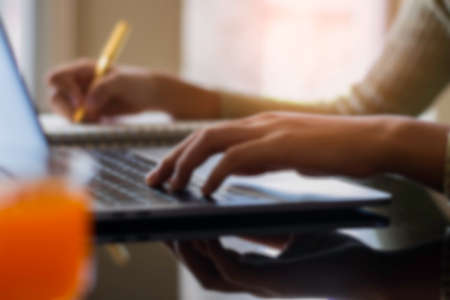 Blurred image of business woman work on laptop computer and writing note on notebook at office....
