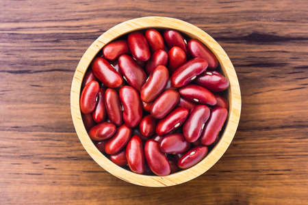 Closeup red beans or kidney bean in wooden bowl isolated on wood table background. Overhead view. Flat lay.の写真素材