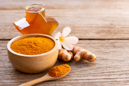 Turmeric ( known as curcumin, Curcuma longa Linn) powder in wooden bowl and glass of honey isolated on old rustic wood table background. Beauty and spa concept.の写真素材