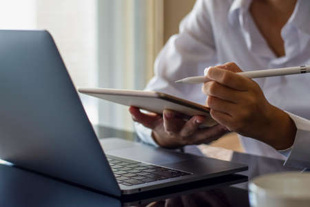 Young asian woman hand holding electronic or stylus pencil and using digital tablet, work on laptop...