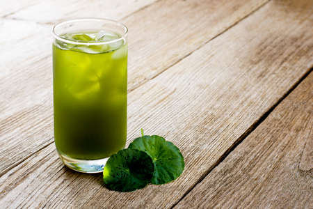 Closeup cup glass of Gotu Kola juice ice tea with green leaves ( Asiatic pennywort, Indian pennywort, Centella asiatica ) isolated on wood table background.の写真素材