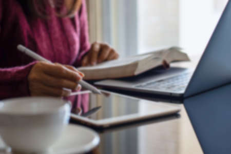 Blurred image of casual woman hand using digital tablet while reading book and work on laptop...