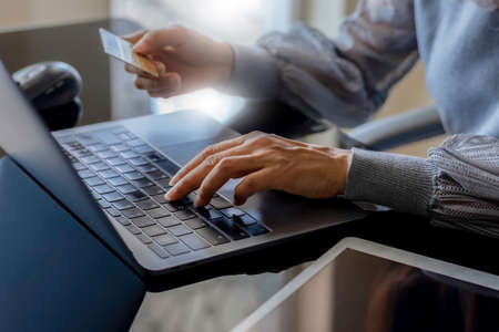 Closeup casual business woman hand holding credit card and typing on laptop computer keyboard for...
