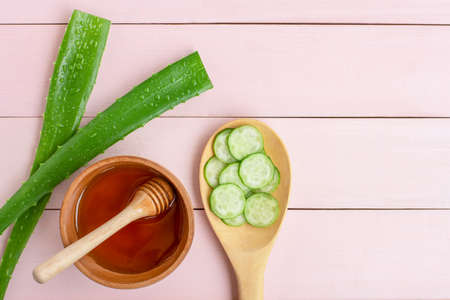 Green fresh aloe vera leaves with water drops, cucumber slice in wooden spoon, honey in bowl isolated on pink wood  table background. Beauty and spa homemade concept. Top view.Flat lay.Space for text.の写真素材