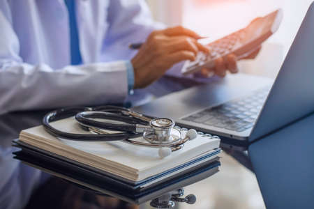 Doctor or practitioner using calculator and work on laptop computer with medical stethoscope  and...