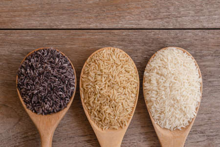Variety type and color of rice ; paddy rice, riceberry ,brown coarse rice and white thai jasmine rice in wooden spoon  isolated on old rustic wood table background. Healthy food concept. Flat lay.の写真素材
