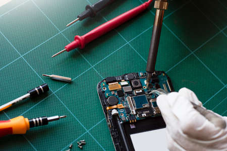 Technician man hand repairing the motherboard of cellphone with forceps and soldering in lab room.の写真素材