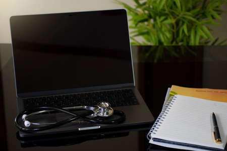Mockup image medical stethoscope on laptop computer with blank screen,notebook and pen on desk at...