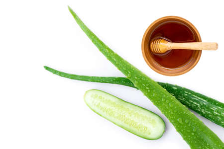 Green fresh aloe vera leaf with water drops and cucumber with honey in wooden bowl isolated on white background. Natural medicine plant,beauty and spa concept. Top viewの写真素材