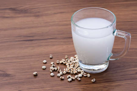 Close up glass of fresh millet milk and white Job's tears ( Adlay millet or pearl millet ) isolated on wood table background. Healthy drinks concept.の写真素材