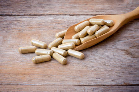 Closeup medicine herbal capsules pill in wooden spoon isolated on old wood table background.の写真素材