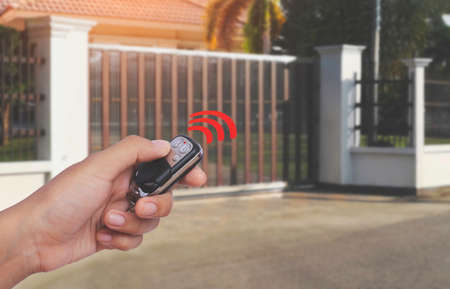Person's hand holding and using remote control to open or close the automatic gate with car parking blurred background. Home remote control and electric door concept.の写真素材