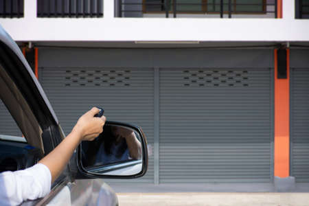 Woman in car, hand holding and using remote control to open the automatic shutter roller steel...