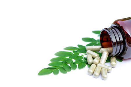 Moringa Oleifera capsule ( Horse radish tree or drumstick, Malunggay ) in brown glass bottle with green leaf isolated on white background. Tropical Thai herbs concept.の写真素材