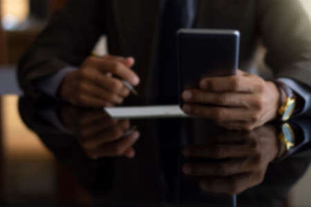 Blurred image of business man in suit using mobile smartphone and plan to write and sign cheque at office.の写真素材