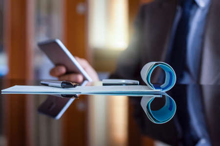 Blurred image of business man in suit using mobile smartphone and plan to write and sign cheque at...