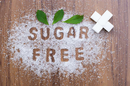 White sugar and words " sugar free " letters written in sugar grains with Stevia leaf isolated on wood table background. Sweetener concept. Top view.の写真素材