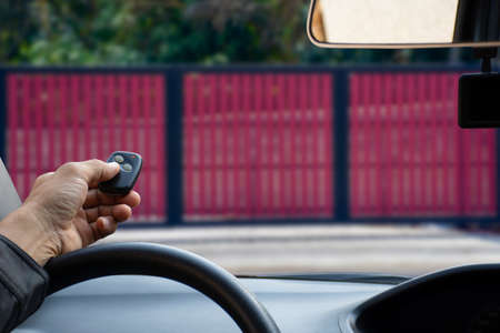 Man in car, hand using remote control to open the automatic door garage. Home remote control and security system  concept.