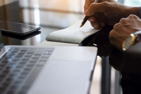 Businessman hand writing and signing bank checkbook with  computer notebook on the desk at office. Payment by check, paycheck, payroll , cheque sign concept.の写真素材