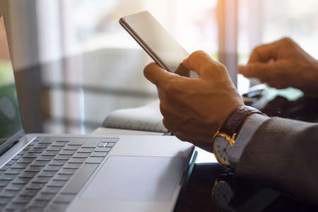 Businessman in suit,  hand holding mobile smart phone, writing and signing checkbook, with laptop...