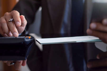 Close up businessman in suit hand using calculator and holding mobile smart phone with check book on...