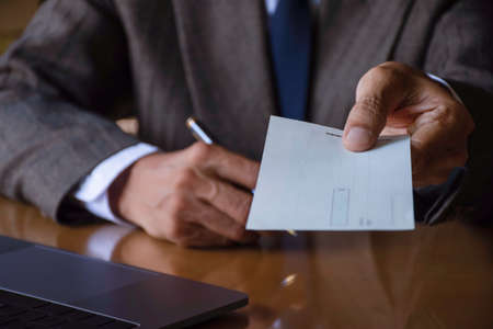 Businessman or manager hand holding pen and giving bank cheque book to the other person. Paycheck and payroll concept.の写真素材