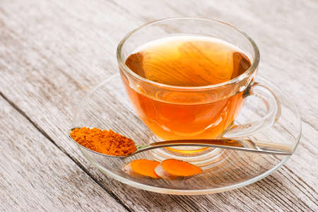 Glass cup of hot Turmeric tea with tumeric powder in wooden spoon isolated on wood board background .の写真素材