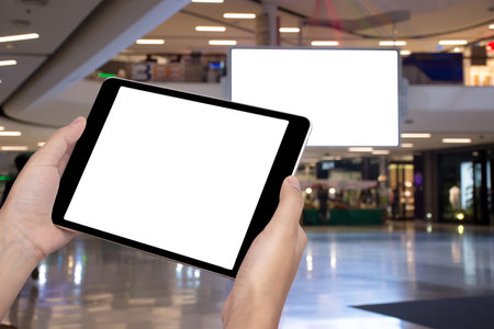 Mockup image of hands holding modern digital tablet with blank billboard ( big television ) in...