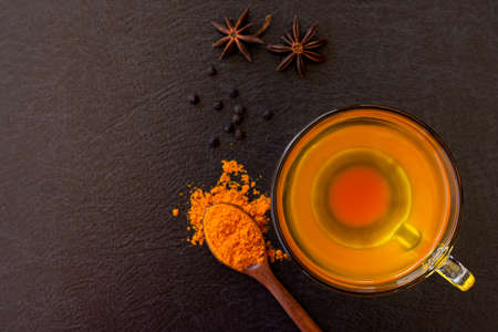 Cup of hot Turmeric tea with tumeric powder and black pepper isolated on dark background .