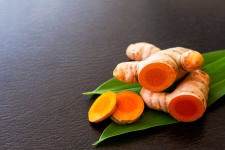 Tumeric ( Turmeric ) root with green leaf and slice isolated on dark table background. Copy space.