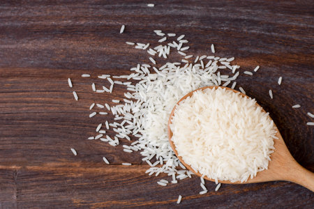 White rice, natural long rice grains ( Thai jasmine rice) in wooden spoon isolated on wooden table background. Top view. flat lay.の写真素材
