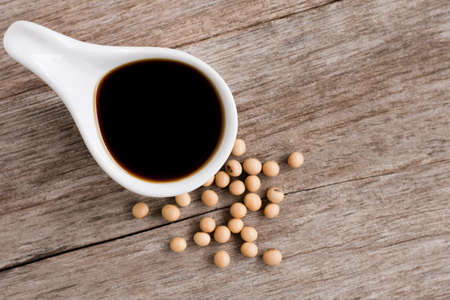 Tasty soy sauce in ceramic bowl with soy beans isolated on wood table background. Top view. Flat...