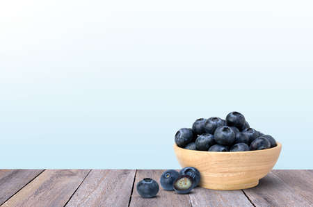 Blueberries fruit in wooden bowl  isolated on wooden table with blue background.の写真素材