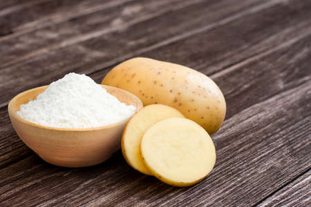Sweet potato powder in wooden bowl and fresh potatoes with slice isolated on wooden table background.の写真素材
