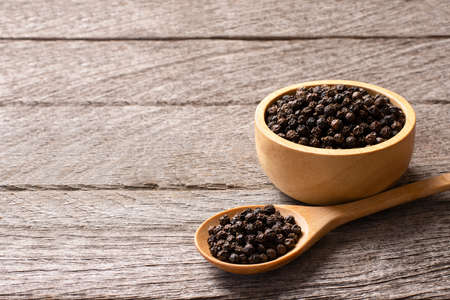 Black pepper in a wooden spoon on a wooden background. Copy space.