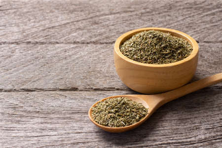 Dried tarragon herb in wooden bowl and spoon on wooden background.
