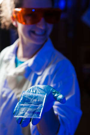 Female researcher in protective glasses holding in hand an agarose gel plate with results of DNA analysisの写真素材