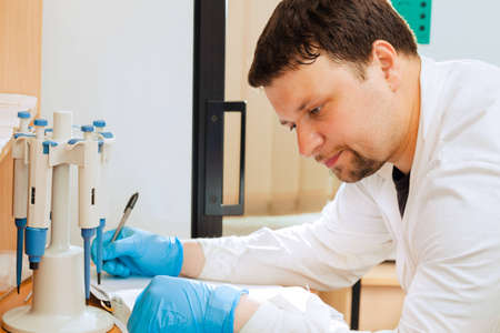 Male scientific researcher writing data into laboratory journalの写真素材