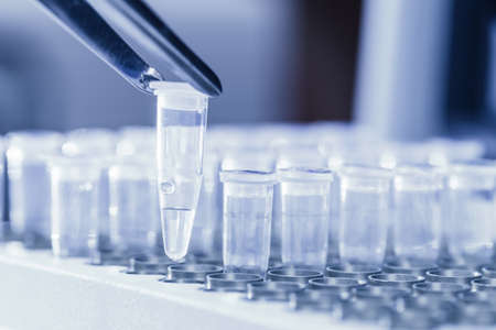 Close-up of tweezers loading test tubes with sampled DNA for polymerase chain reaction  Blue toned imageの写真素材