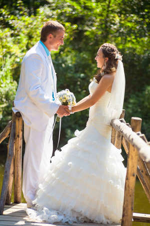 Happy bride and groom smiling and holding by hands with bouquetの写真素材